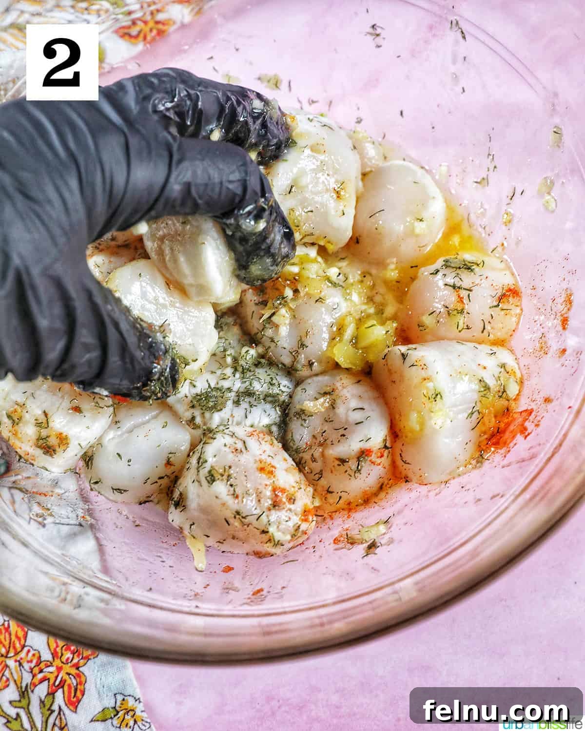 Golden Air Fryer Scallops 6 a gloved hand mixing together scallops with herbs and spices in a clear glass bowl.