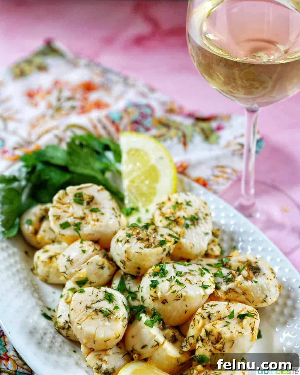 Golden Air Fryer Scallops 9 several cooked scallops topped with herbs and garlic, with lemon slices and parsley, on a white plate with a glass of white wine next to it.