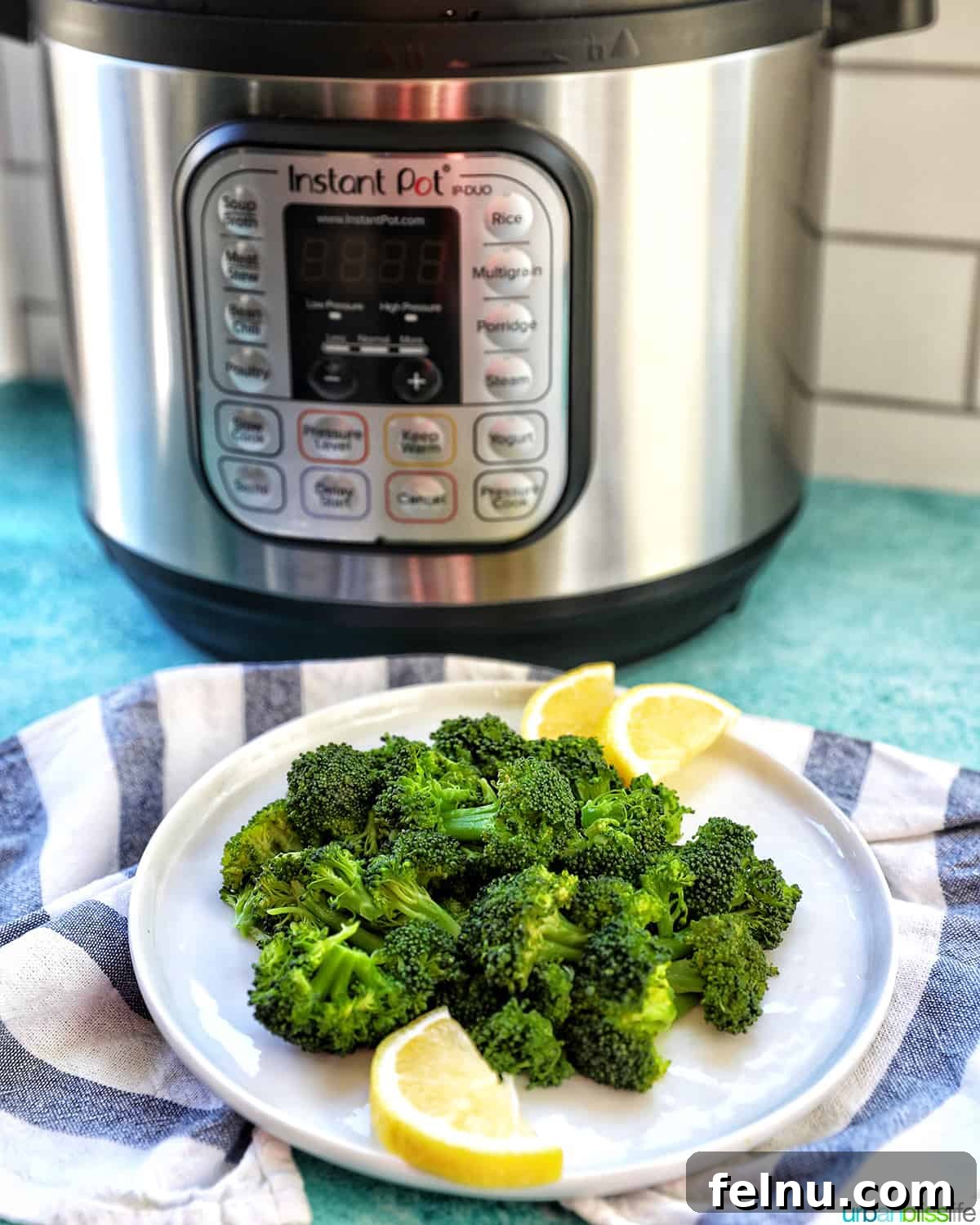 Perfect Instant Pot Broccoli 11 pressure cooked broccoli in a plate with lemon wedges with an Instant Pot pressure cooker behind.