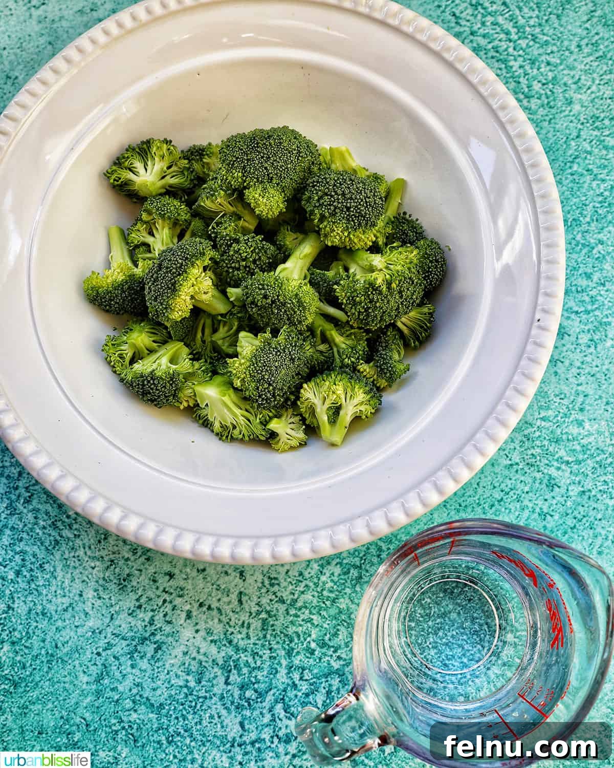Perfect Instant Pot Broccoli 4 bowl of broccoli florets next to a cup of water on a blue table.