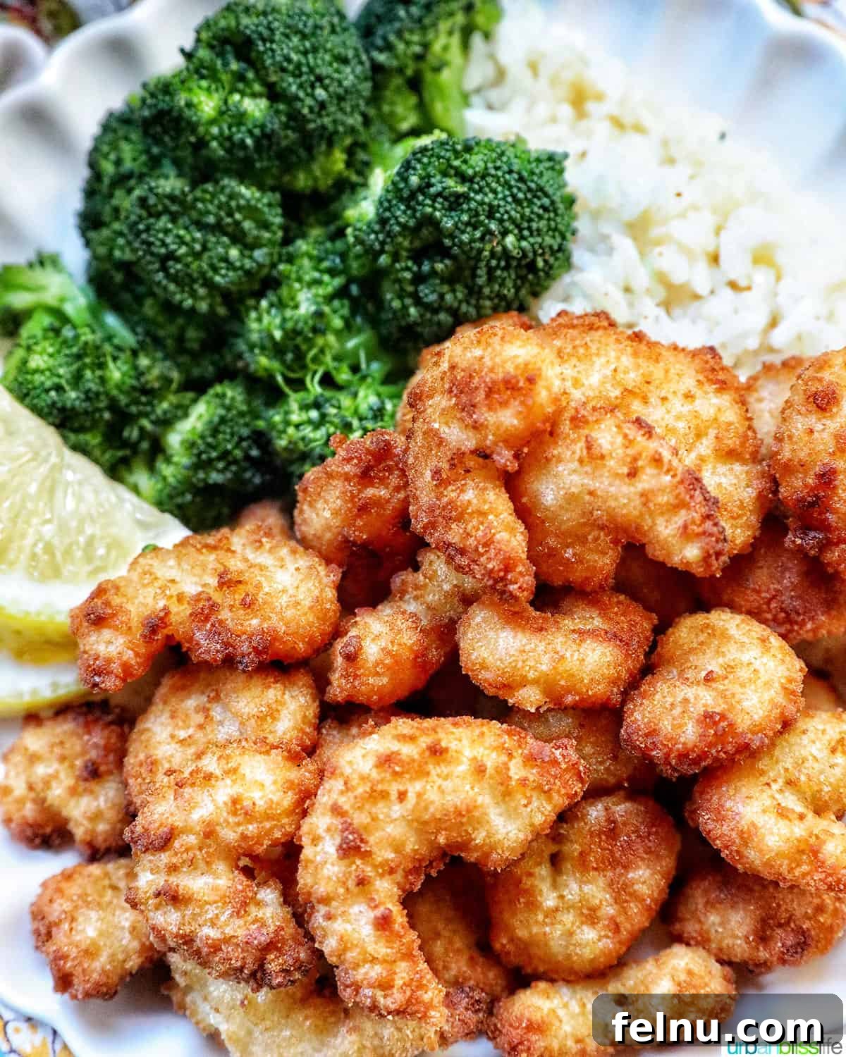 Crispy Air Fryer Popcorn Shrimp 3 A close-up shot of perfectly golden air-fried popcorn shrimp on a plate, garnished with fresh lemon wedges and a side of vibrant green broccoli.