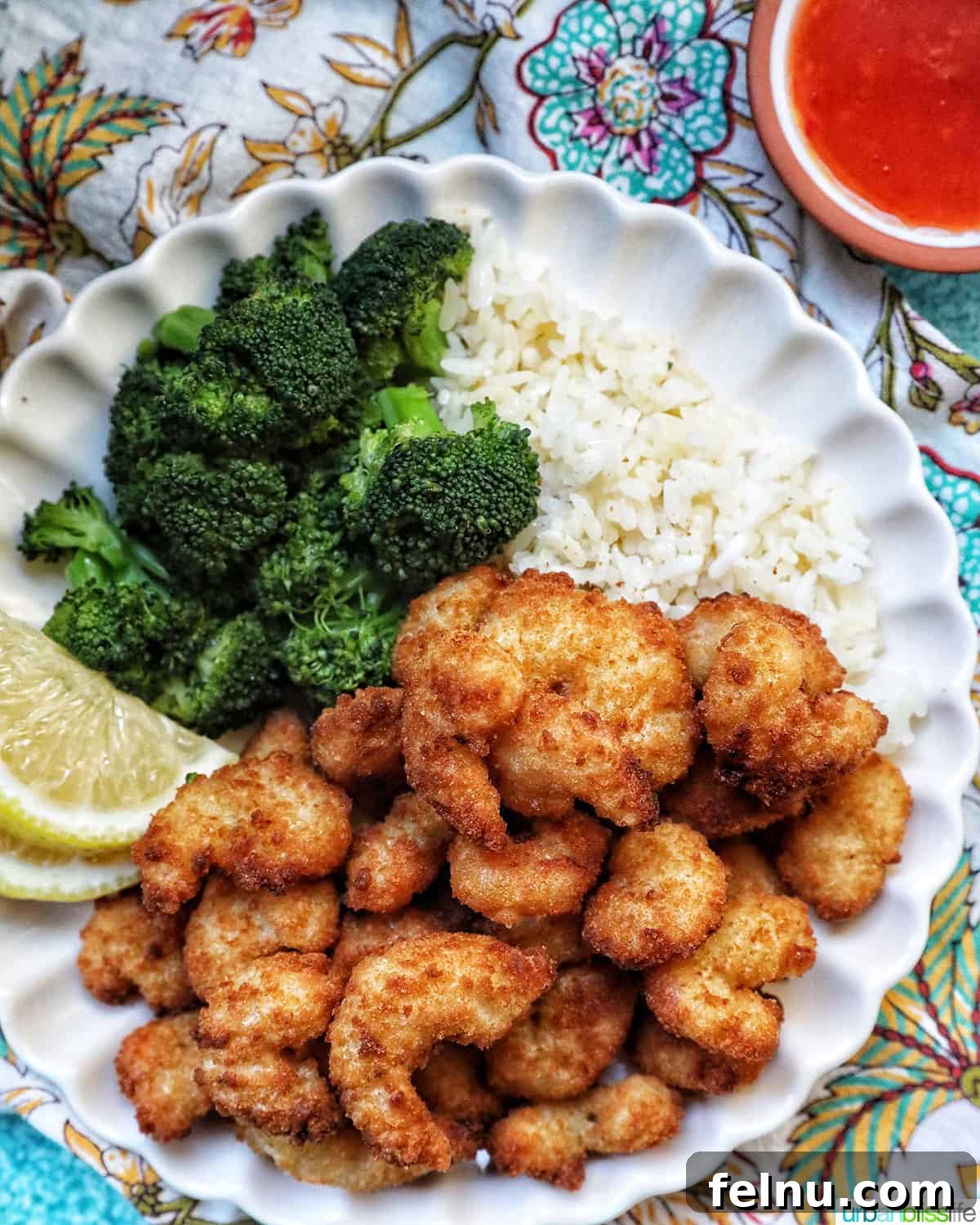 Crispy Air Fryer Popcorn Shrimp 9 A vibrant plate of crispy air fryer popcorn shrimp, accompanied by steamed broccoli, fresh lemon wedges, and a ramekin of cocktail sauce.
