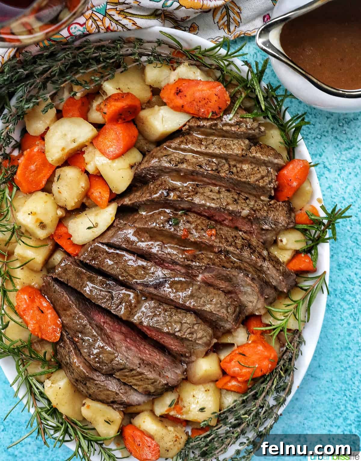 Tender Instant Pot Sirloin Tip Roast 2 serving plate with cooked sirloin tip roast surrounded by carrots, potatoes, and herbs with a side of gravy.