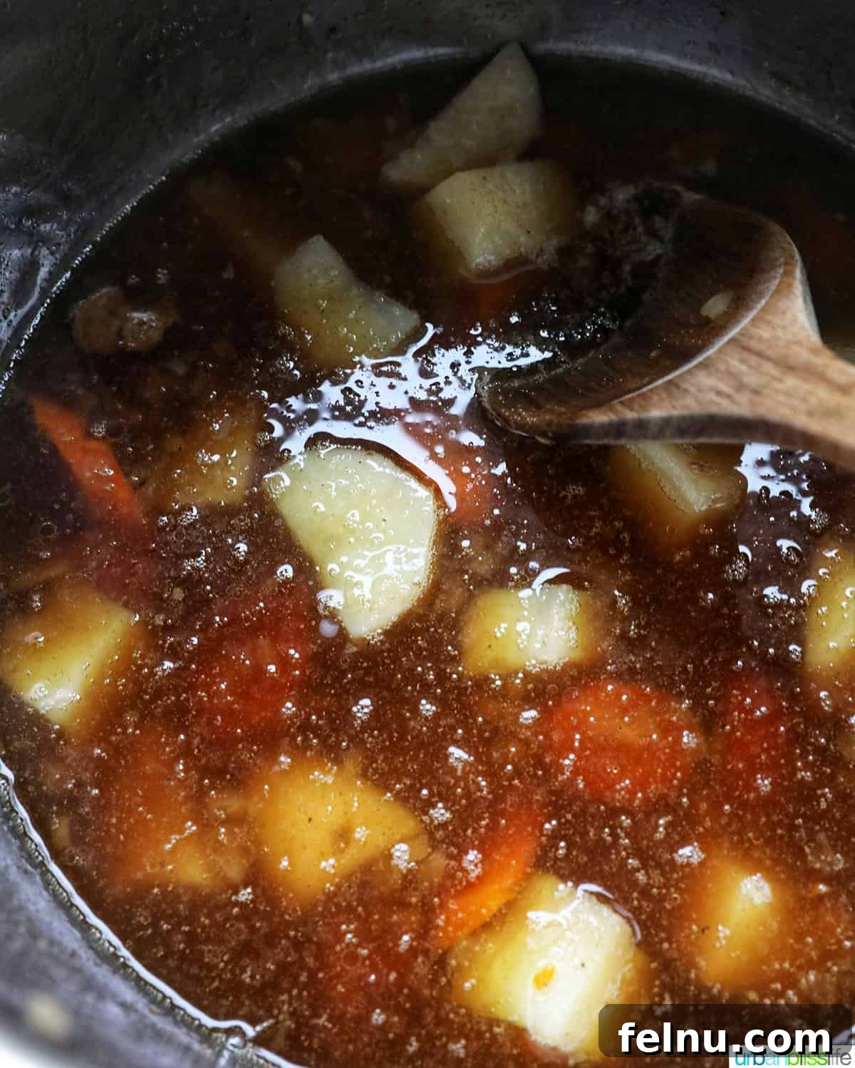 Tender Instant Pot Sirloin Tip Roast 15 wooden spoon stirring potatoes and carrots in beef broth in an Instant Pot electric pressure cooker.