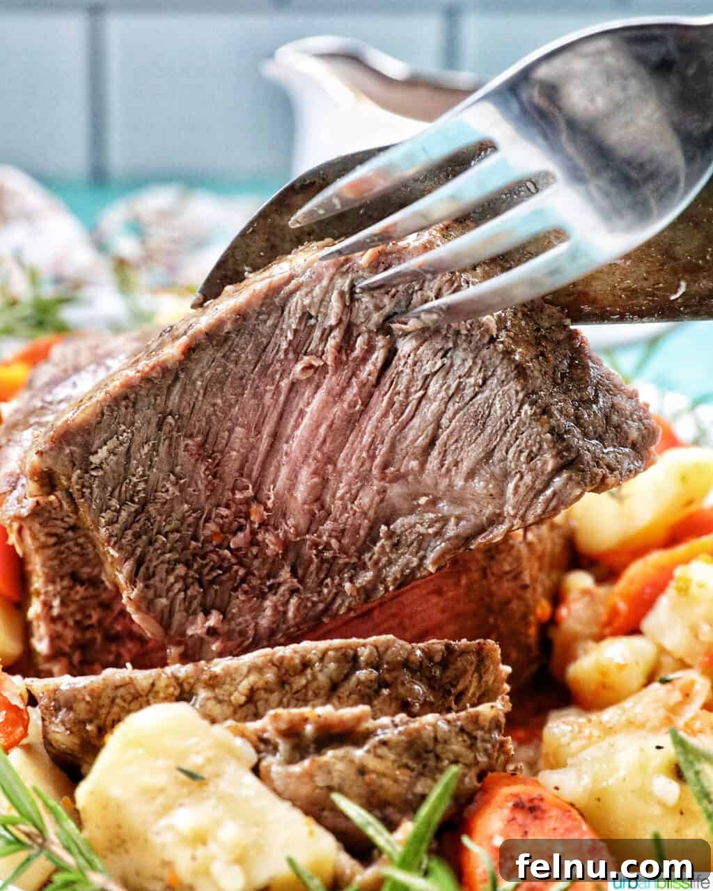 Tender Instant Pot Sirloin Tip Roast 20 Large fork and knife holding up a slice of sirloin tip roast with potatoes and carrots in front.