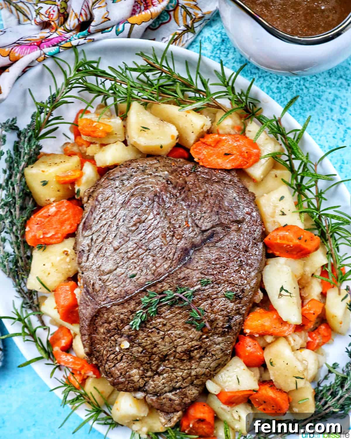 Tender Instant Pot Sirloin Tip Roast 3 serving plate with cooked sirloin tip roast surrounded by carrots, potatoes, and herbs with a side of gravy.