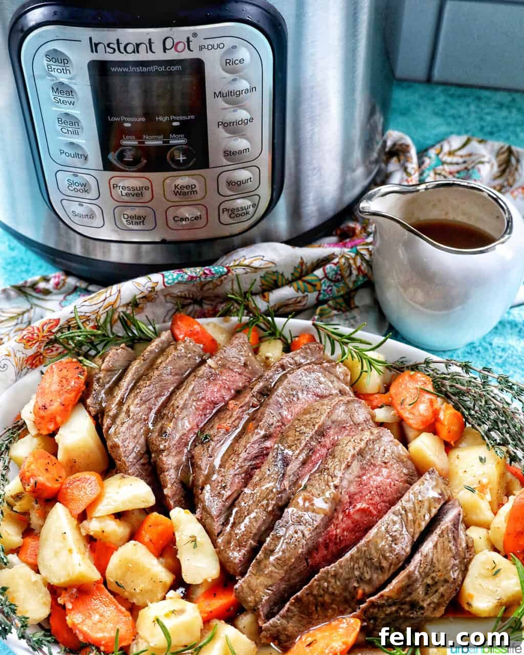 Tender Instant Pot Sirloin Tip Roast 22 Sliced sirloin tip roast surrounded by carrots, potatoes, and herbs in front of an Instant Pot with a side of gravy.