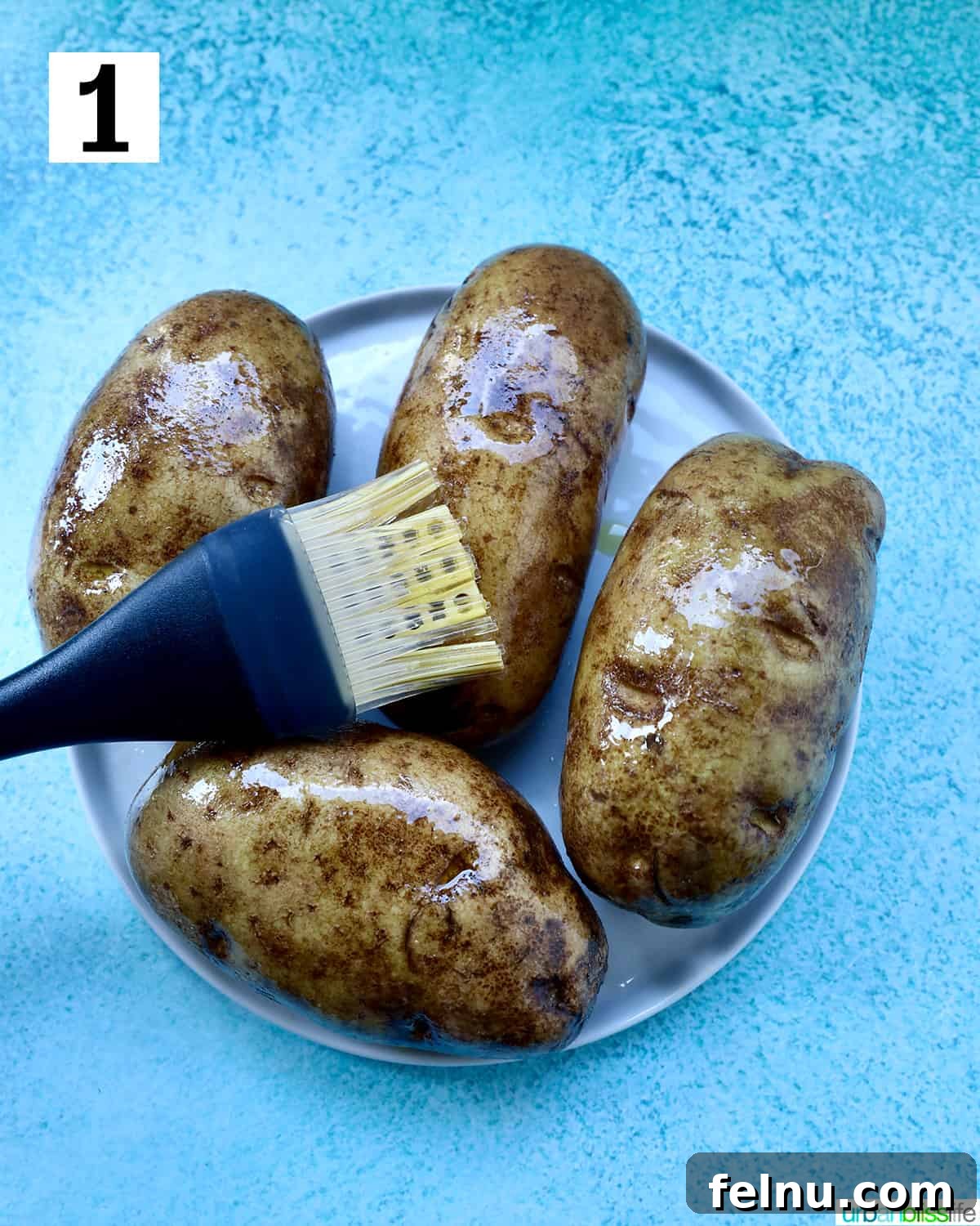 Crispy Fluffy Ninja Foodi Air Fryer Baked Potatoes 5 pastry brush brushing olive oil on potatoes on a plate.