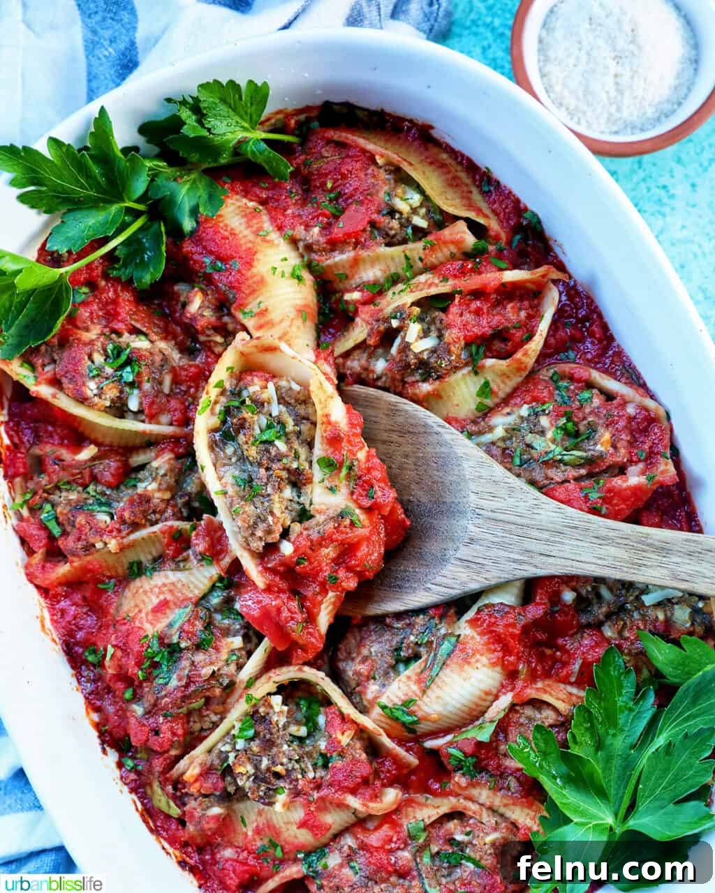 Hearty Dairy-Free Beef Stuffed Shells 13 A wooden spoon lifting a single perfectly cooked stuffed shell with ground beef, dripping with sauce, over a full casserole dish.