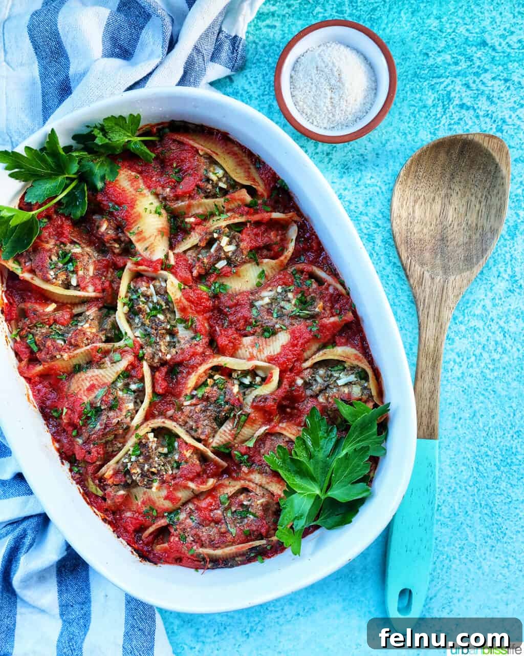 Hearty Dairy-Free Beef Stuffed Shells 14 A beautiful casserole dish of stuffed shells with ground beef, accompanied by a wooden spoon and a side of dairy-free parmesan cheese, ready to serve.