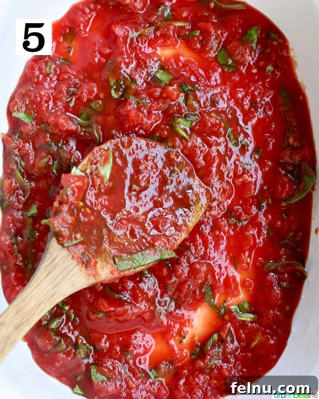Hearty Dairy-Free Beef Stuffed Shells 9 A wooden spoon carefully spreading a layer of marinara sauce evenly across the bottom of a casserole dish.