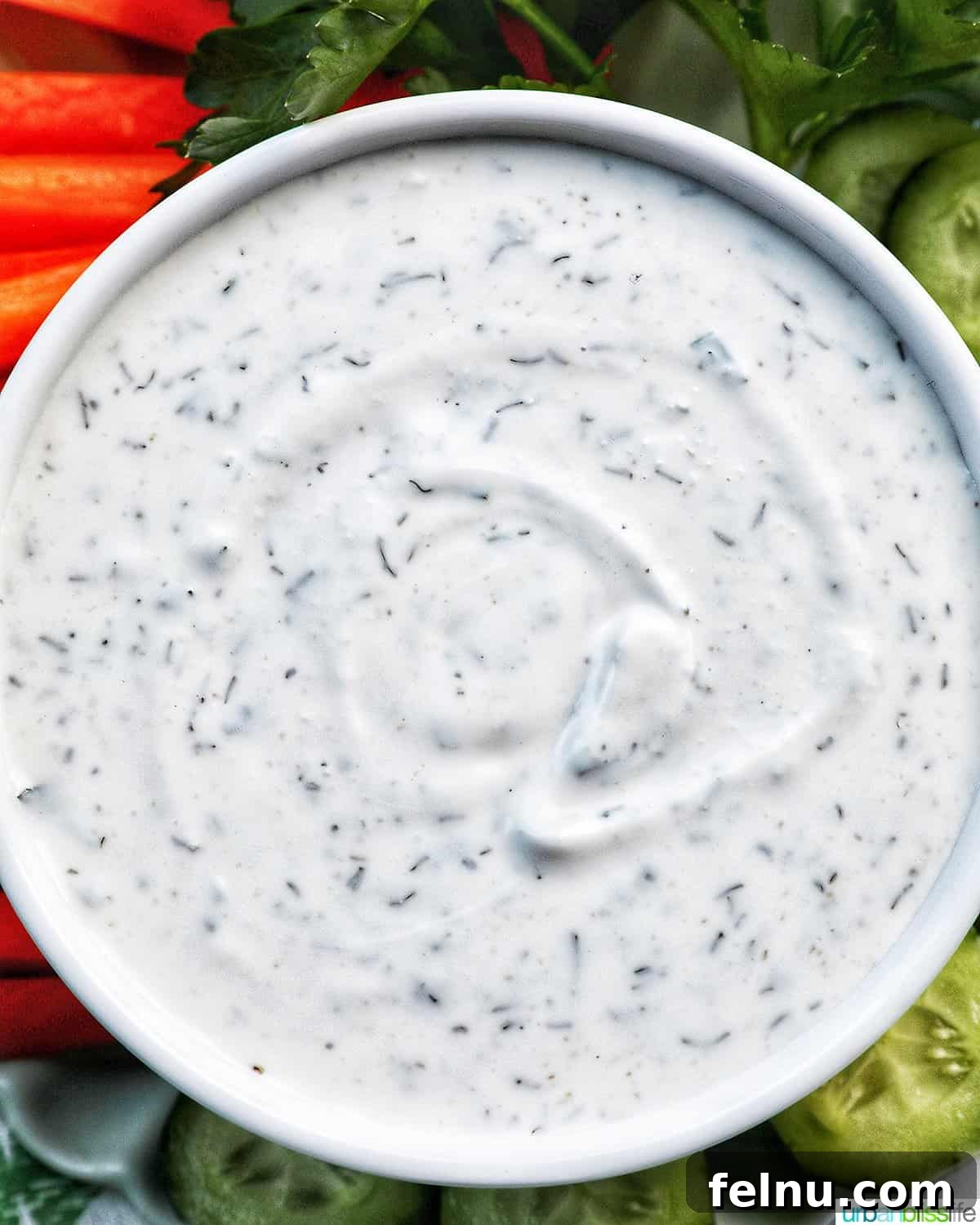 A close-up shot of the creamy homemade Dairy-Free Ranch Dressing, inviting you to dip a crisp vegetable stick into its rich texture, with fresh herbs scattered around.