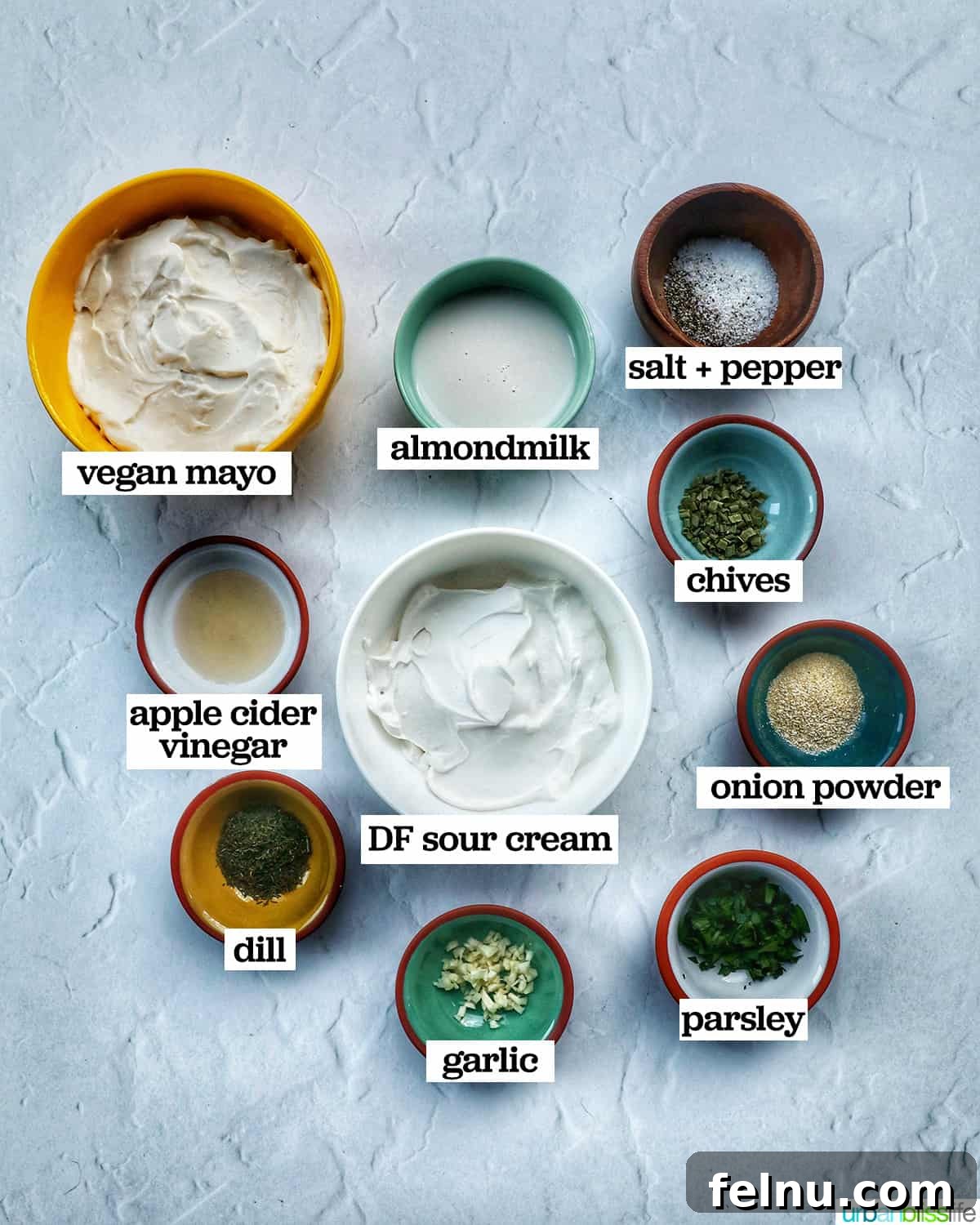 Individual bowls holding various ingredients like mayonnaise, sour cream, fresh herbs, and spices, all set to be combined into a dairy-free ranch dressing.