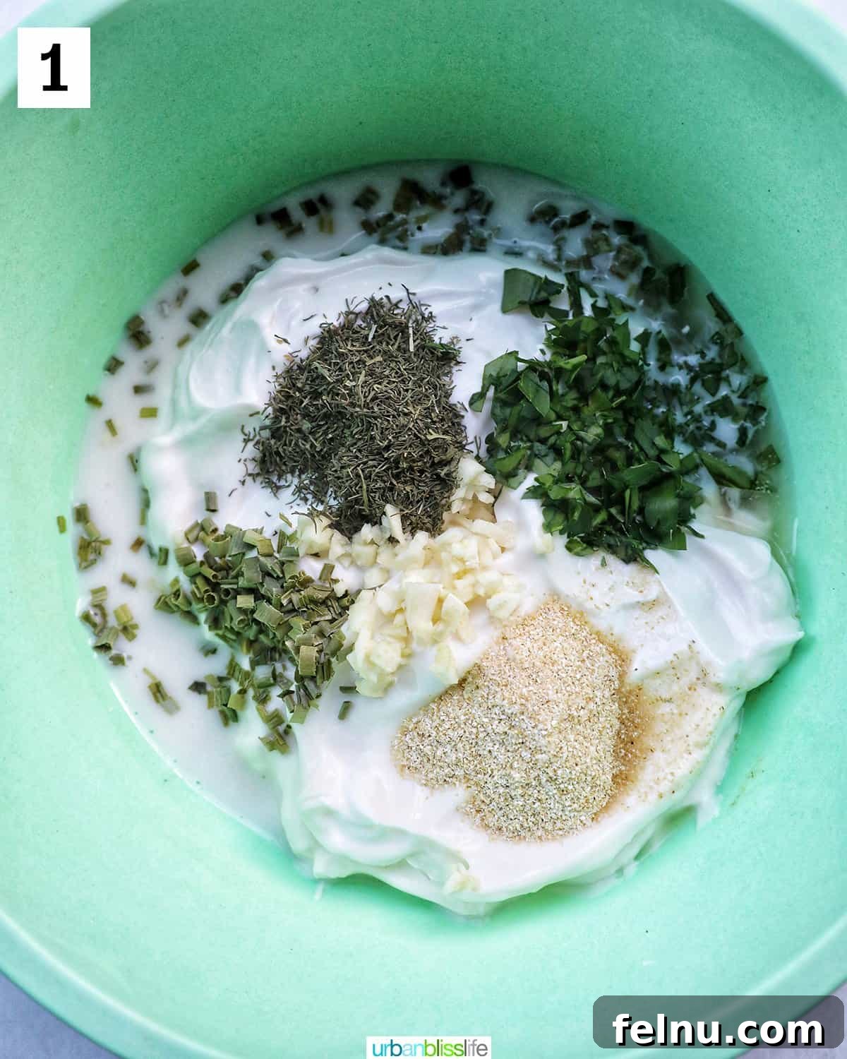 A green mixing bowl filled with the base ingredients for dairy-free ranch dressing: mayonnaise, sour cream, minced garlic, and fresh herbs.