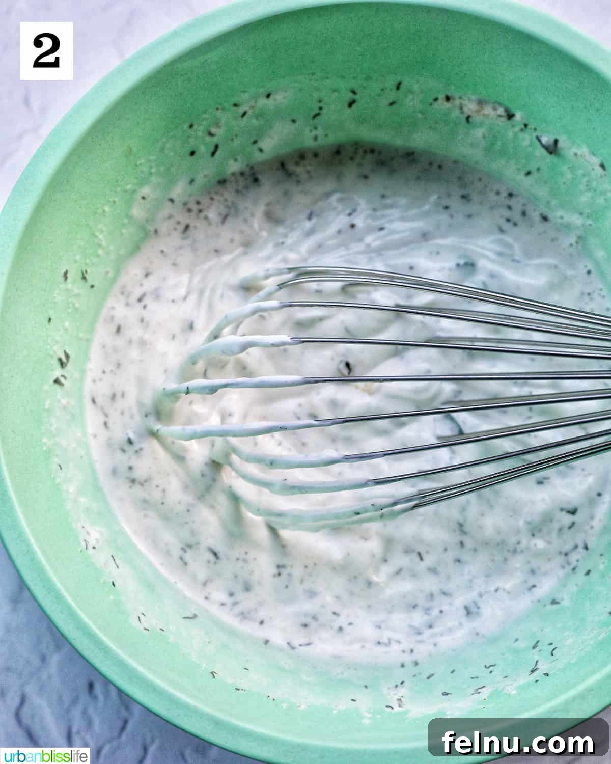 A whisk vigorously mixing all the ingredients together in a green bowl to create a smooth and creamy homemade dairy-free ranch dressing.