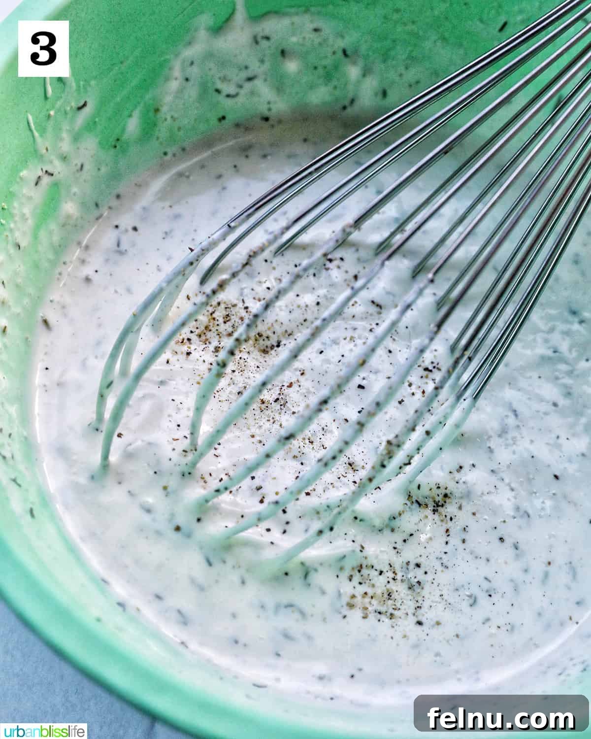 The whisk still in the green bowl of dairy-free ranch dressing, with a shaker of salt and a pepper mill nearby, indicating the final seasoning step.
