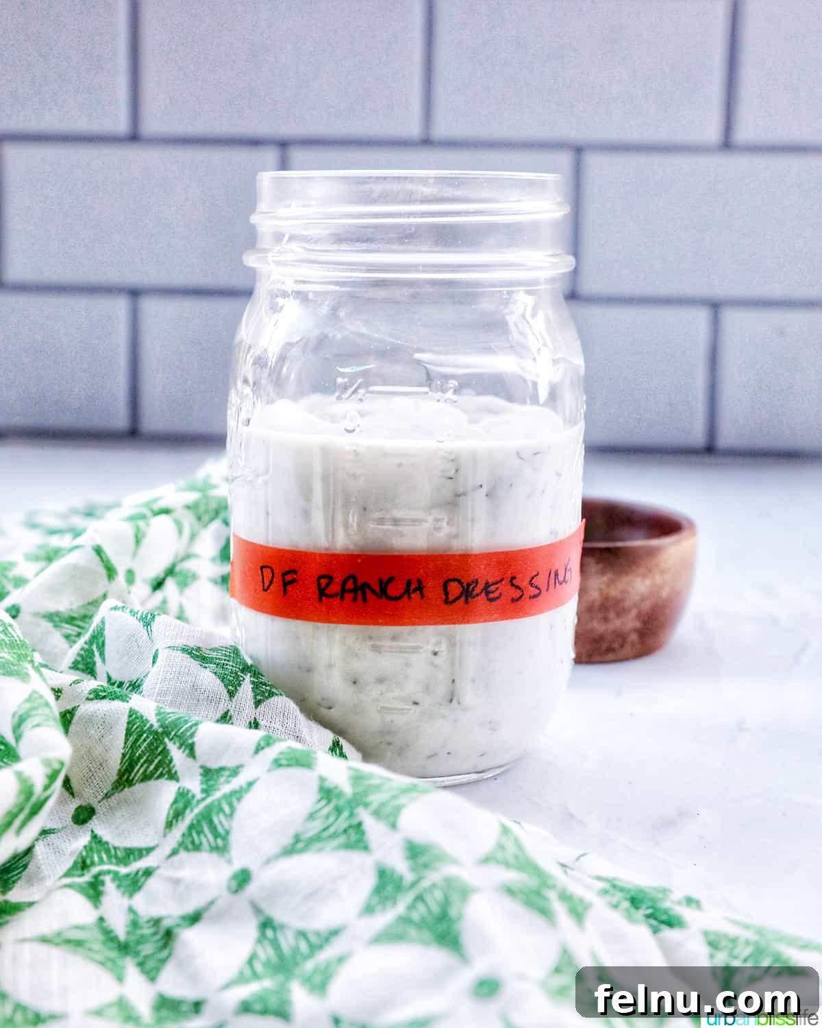 A mason jar filled with homemade dairy-free ranch dressing, adorned with a label and placed on a green and cream napkin, emphasizing its freshness and homemade quality.