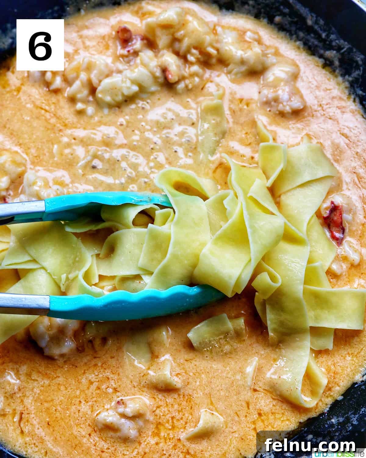 Luxurious Lobster Pasta 12 blue tongs adding pappardelle pasta to lobster sauce in a pan.