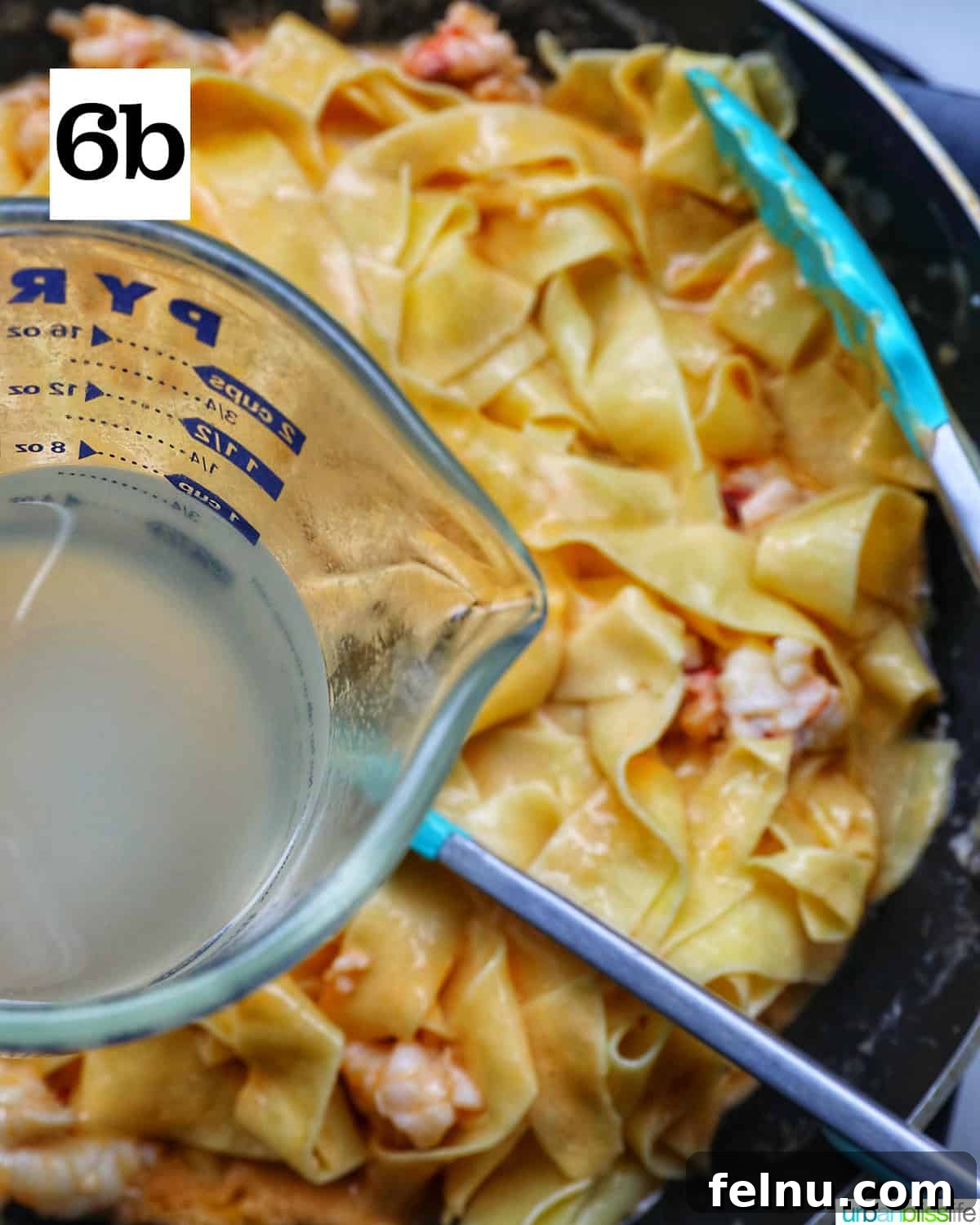 Luxurious Lobster Pasta 13 glass measuring cup with starchy pasta water over a pan of pappardelle pasta.