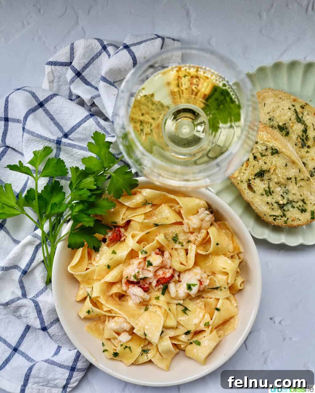 Luxurious Lobster Pasta 15 bowl of lobster pasta with side of parsley, with a glass of white wine and garlic bread.