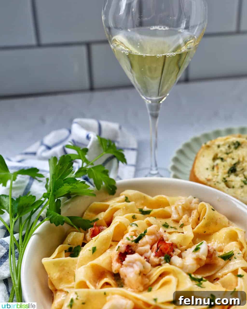 Luxurious Lobster Pasta 16 bowl of lobster pasta with side of parsley and a glass of white wine.