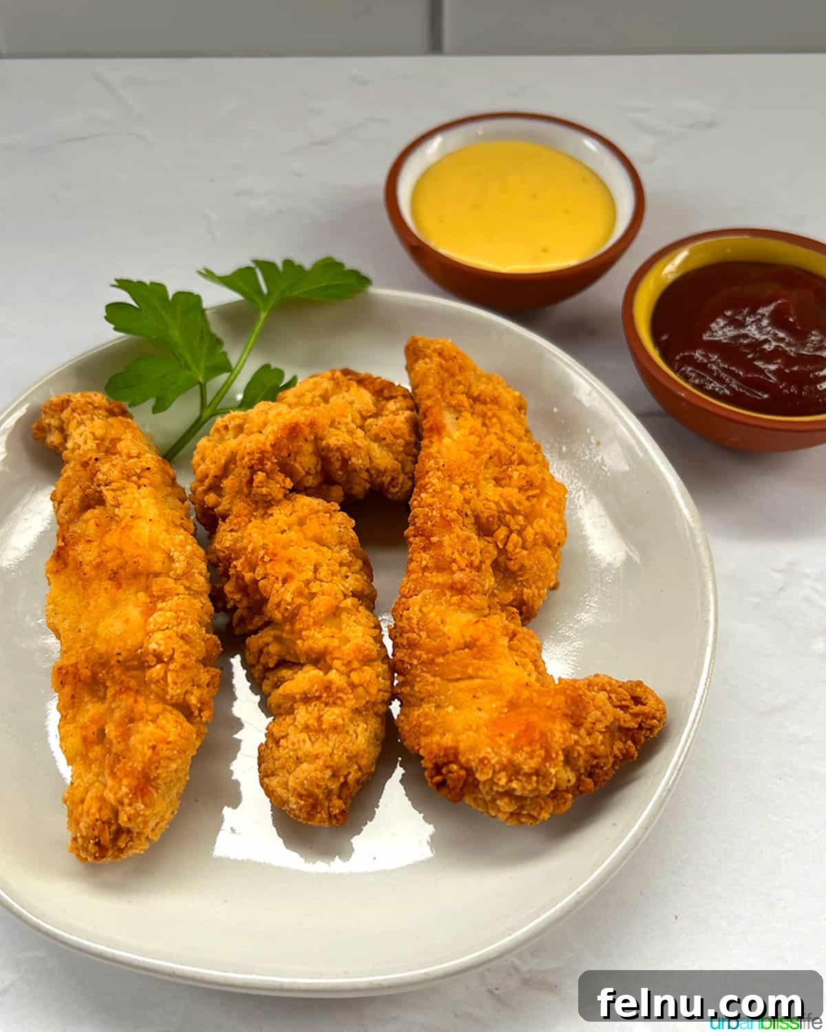 Air Fryer Frozen Chicken Tenders Made Perfect 2 Crispy air fryer frozen chicken tenders served on a plate with honey mustard and barbecue dipping sauces.