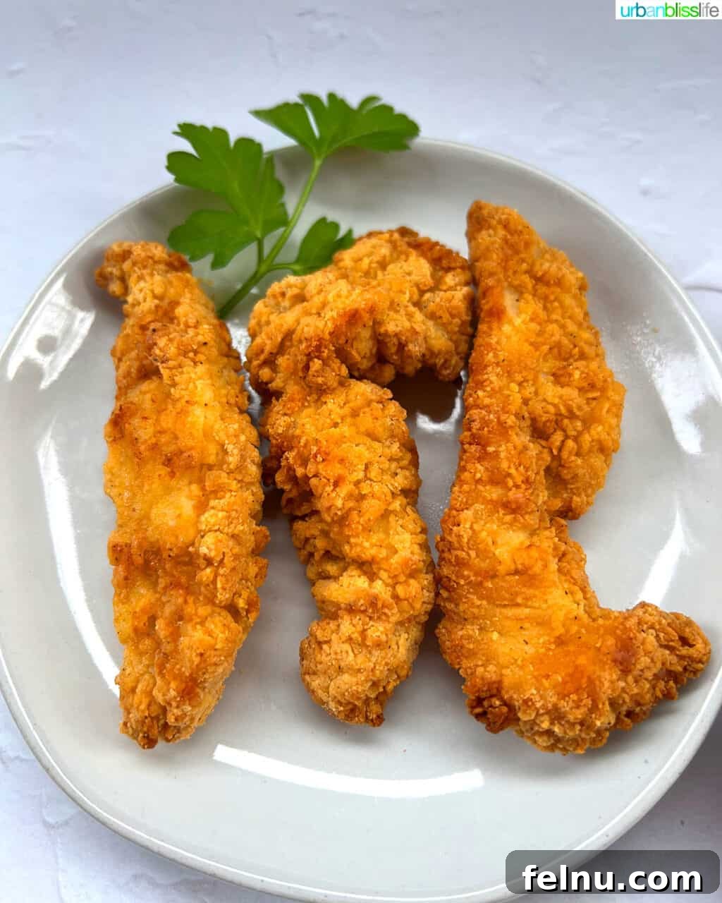 Air Fryer Frozen Chicken Tenders Made Perfect 3 Freshly cooked air fryer chicken tenders garnished with parsley on a white plate, ready to be served.
