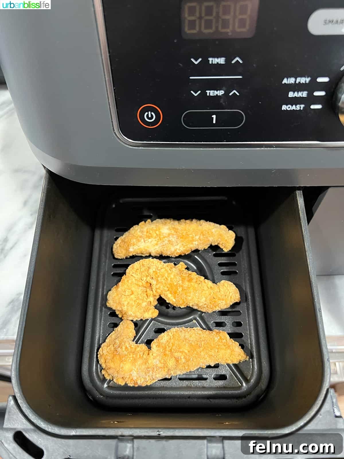 Air Fryer Frozen Chicken Tenders Made Perfect 5 Frozen chicken tenders being placed into an air fryer basket in a single layer.