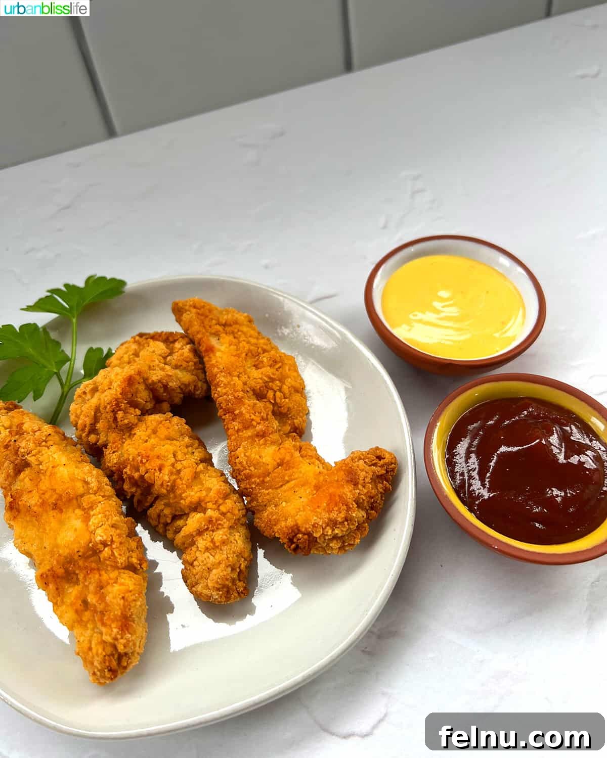 Air Fryer Frozen Chicken Tenders Made Perfect 8 Air fryer frozen chicken tenders arranged on a plate with small bowls of honey mustard and barbecue sauce.
