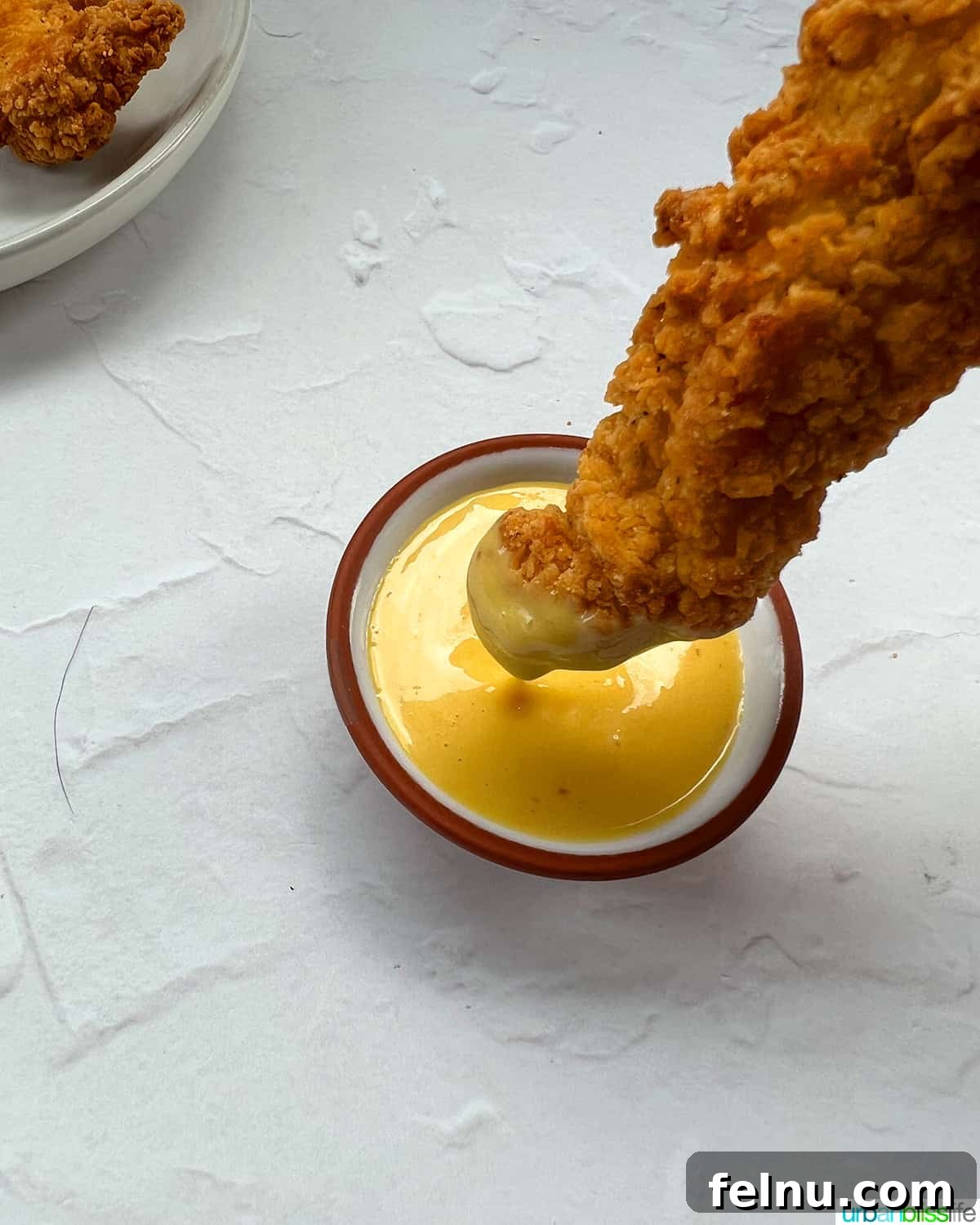 Air Fryer Frozen Chicken Tenders Made Perfect 9 A crispy air fryer frozen chicken tender being dipped into a bowl of creamy honey mustard sauce.