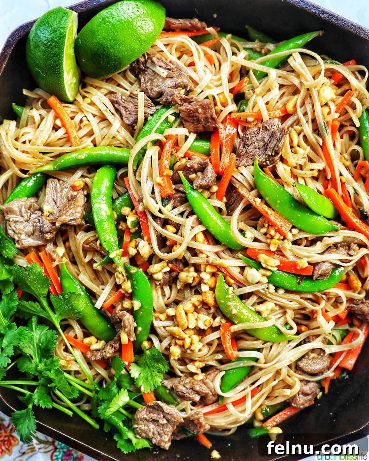 Beef Pad Thai 2 Beef Pad Thai noodles with vegetables, lime wedge, and parsley in a cast iron skillet.