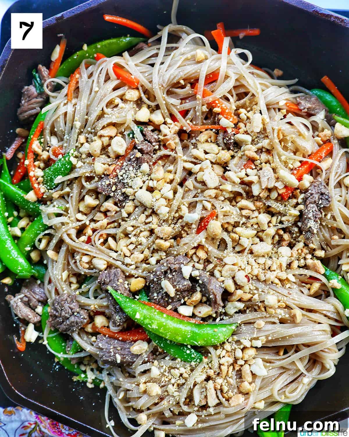 Beef Pad Thai 12 Adding crushed peanuts to beef pad thai noodles with vegetables in a skillet.