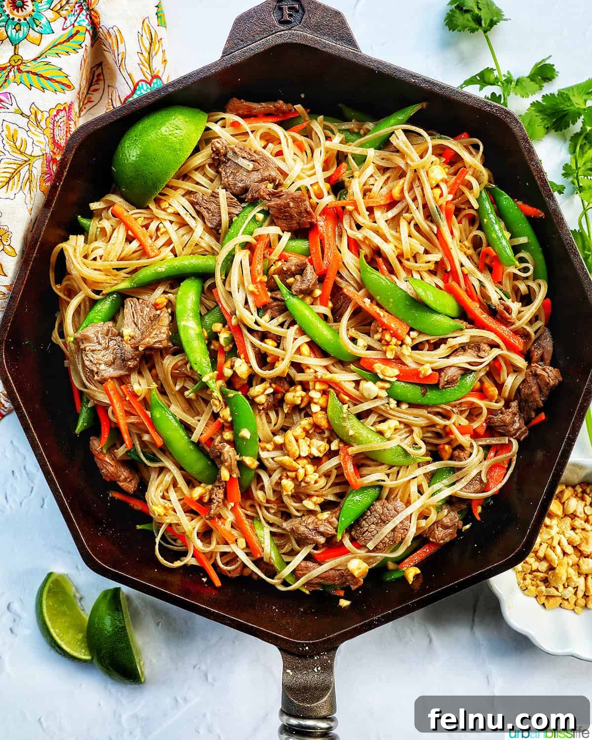 Beef Pad Thai 13 Beef pad thai noodles with vegetables in a Finex cast iron skillet with side of lime wedges and chopped peanuts.