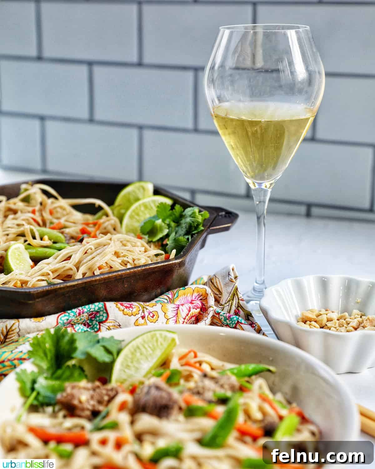 Beef Pad Thai 15 Bowl of beef pad thai noodles with vegetables with glass of white wine and skillet of more pad thai.