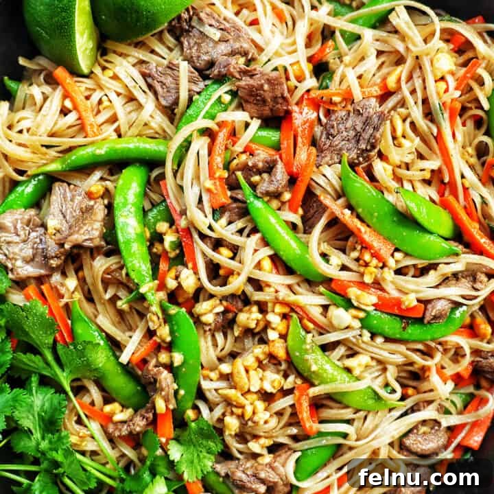 Closeup of beef pad thai noodles with vegetables in a skillet with side of parsley.