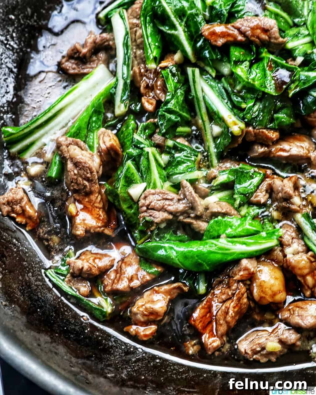 Savory Thai Beef Pad See Ew Noodles 13 A close-up shot of beef and bok choy cooking in a wok, covered in a rich, dark sauce, illustrating the stir-frying process.