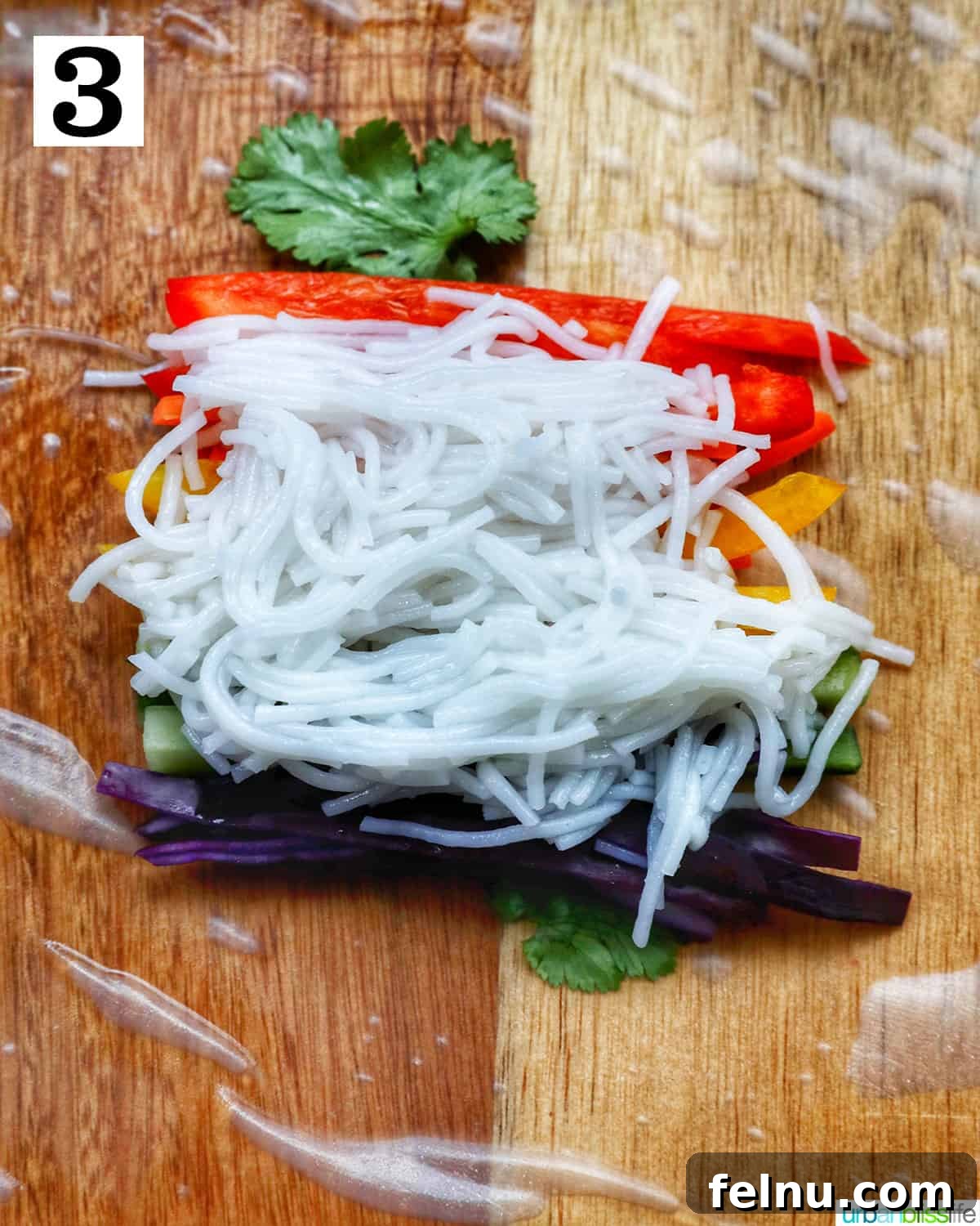 Vegan Delight: Fresh Summer Rolls 7 A rice paper roll topped with vermicelli rice noodles and a vibrant mix of sliced colorful vegetables on a wooden cutting board, showcasing the complete filling before rolling.