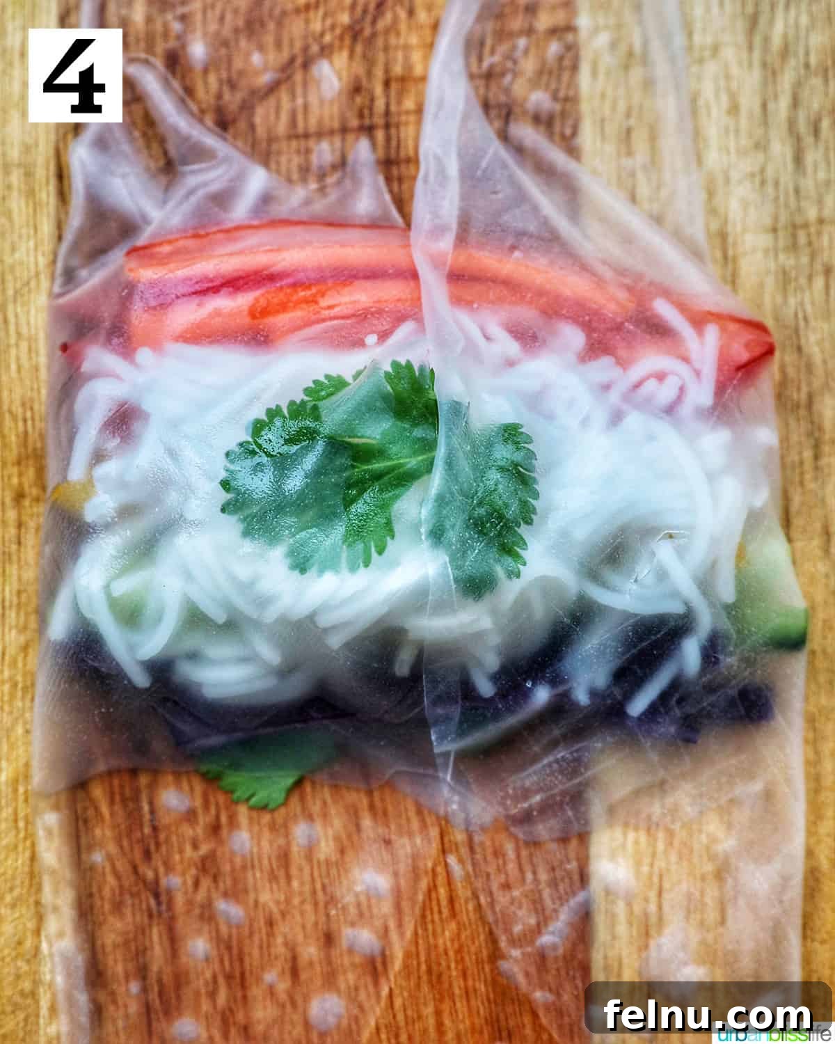 Vegan Delight: Fresh Summer Rolls 8 A rice paper roll topped with vermicelli rice noodles and sliced colorful vegetables on a wooden cutting board, ready to be carefully folded and rolled.