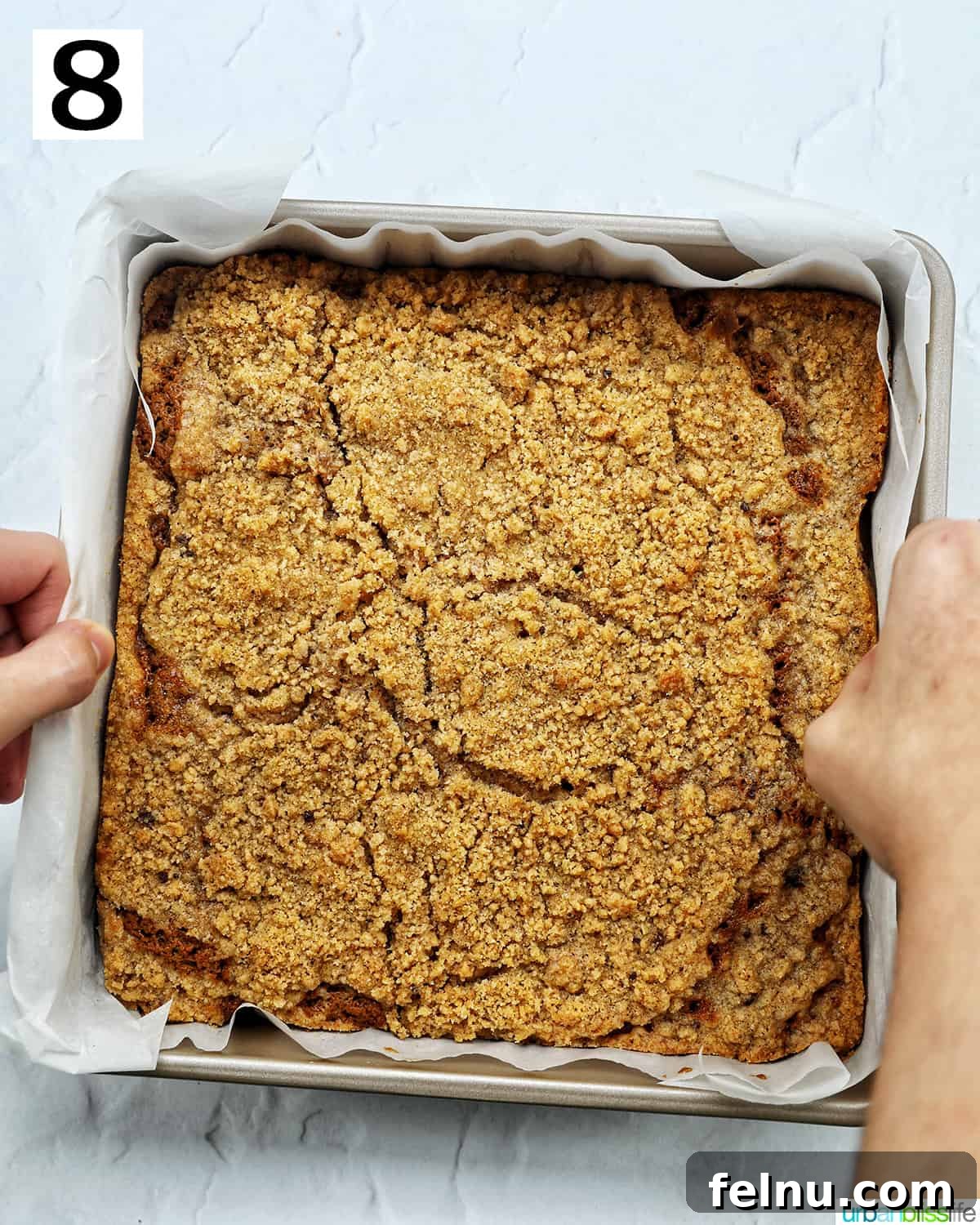 Emerald Isle Coffee Cake 17 Hands gently lifting the baked Irish coffee cake, supported by parchment paper, out of the baking pan, ready to cool.