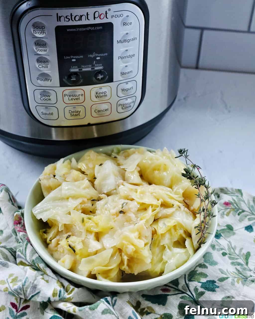 Effortless Instant Pot Cabbage 12 A serving bowl of cooked Instant Pot Cabbage with thyme sprigs, positioned in front of a modern Instant Pot pressure cooker.