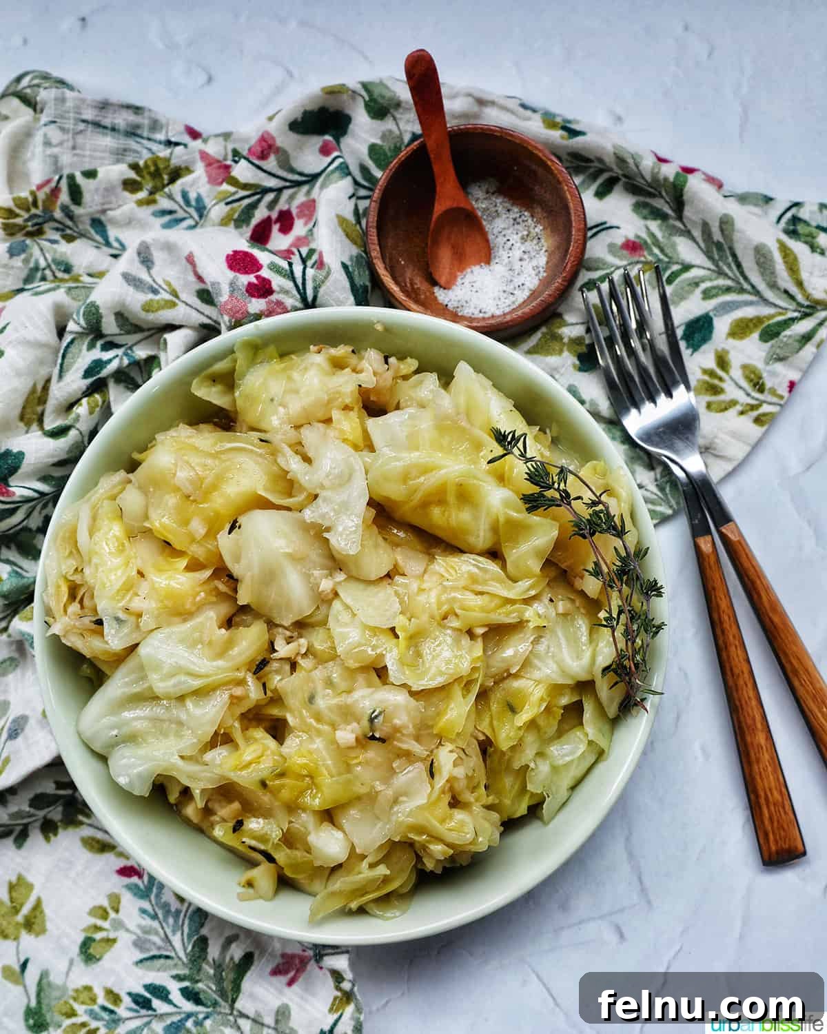 Effortless Instant Pot Cabbage 3 An inviting overhead view of a bowl of cooked Instant Pot Cabbage, garnished with fresh thyme, alongside a fork and small bowls of salt and pepper.