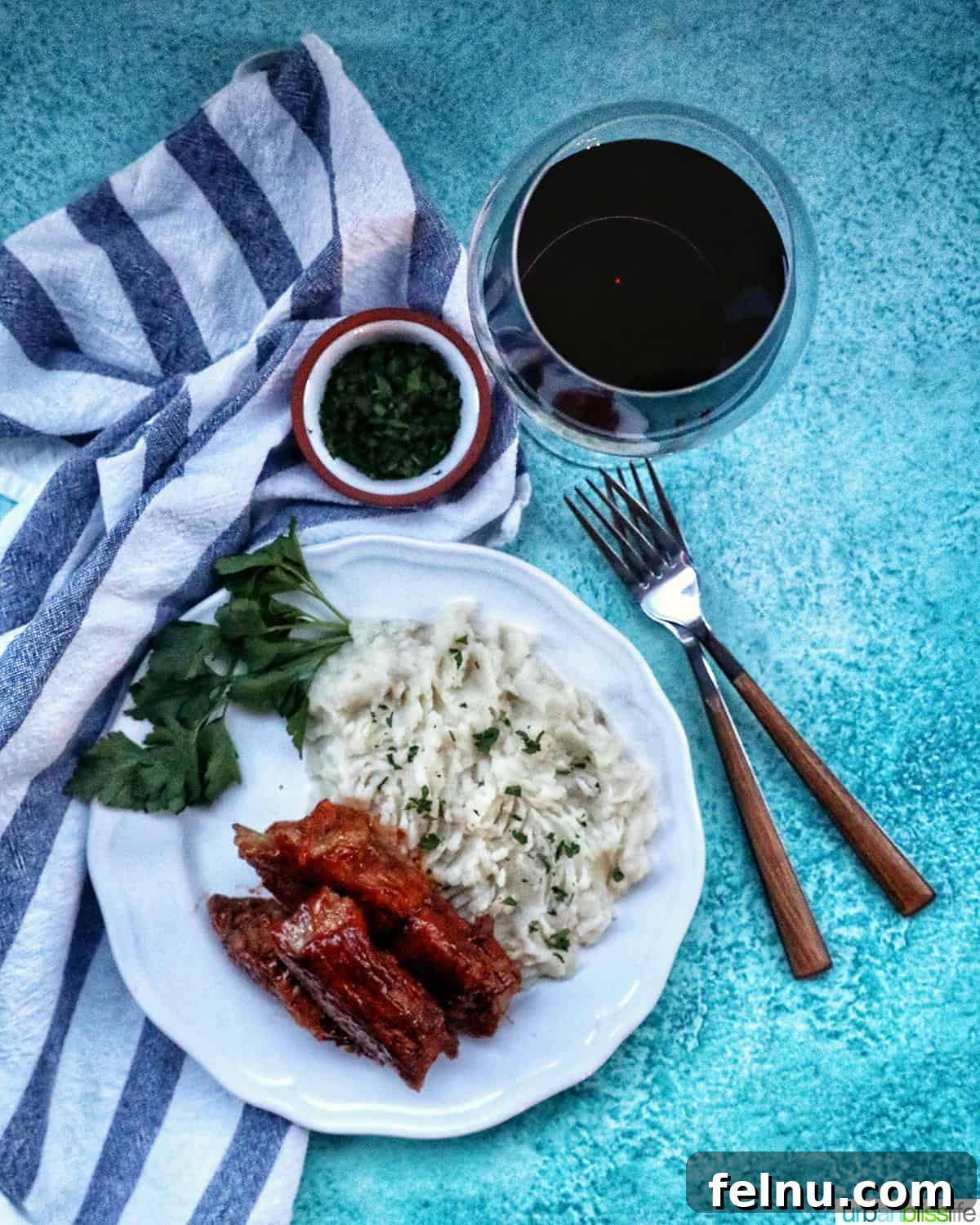 Country style ribs and mashed potatoes on a white plate with forks and red wine.
