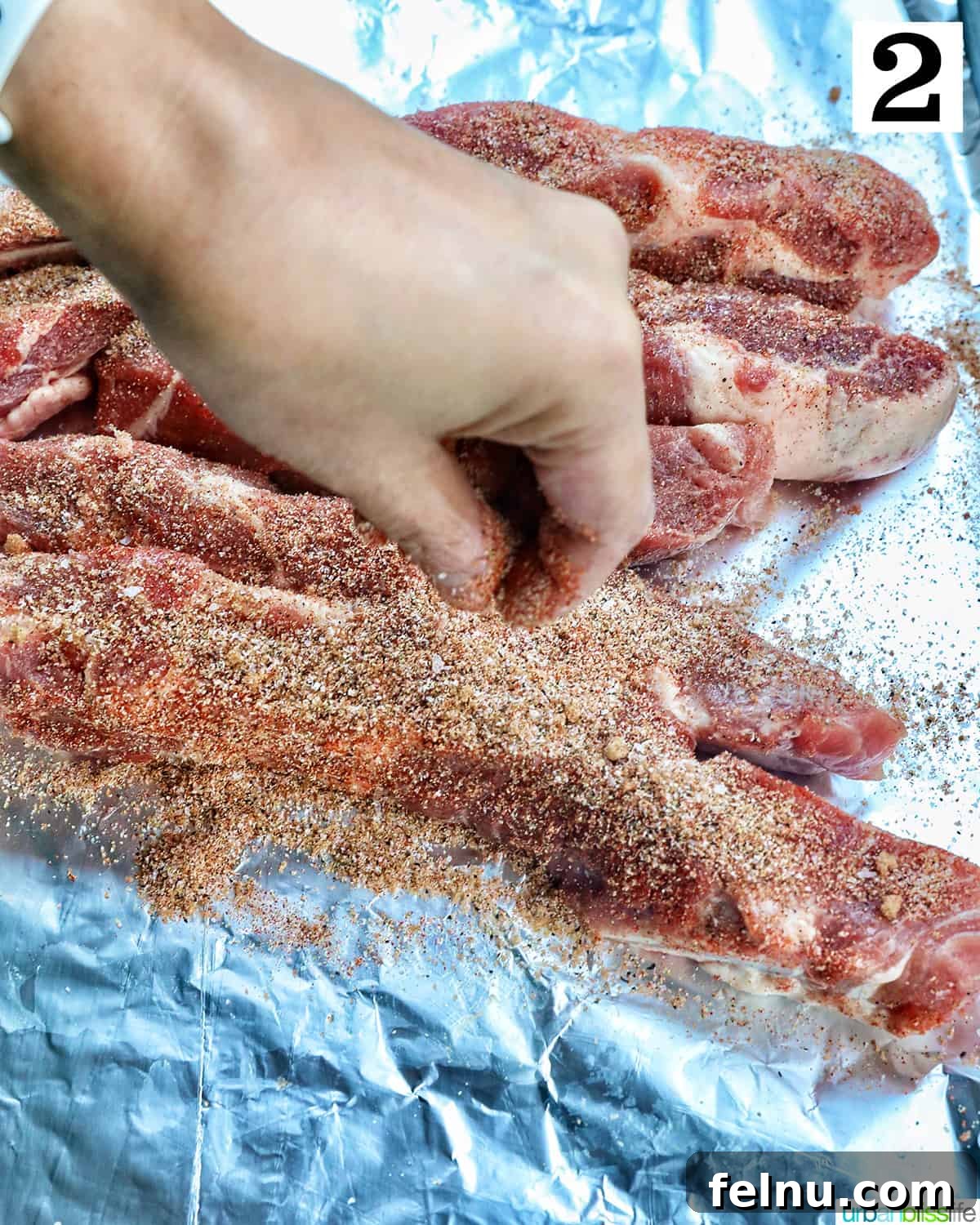 Hand seasoning ribs on aluminum foil.