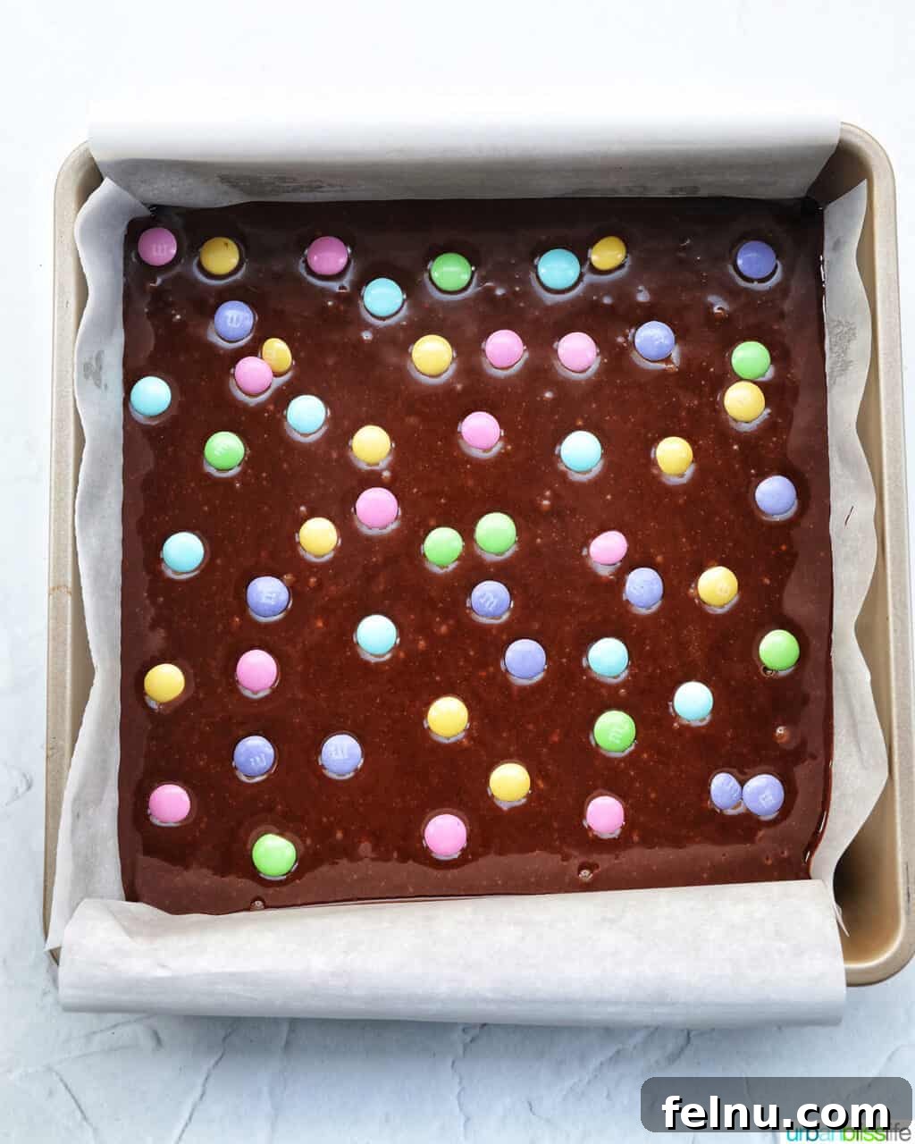 Easter Chocolate Squares 15 Brownie batter in a square baking pan, generously dotted with pastel Easter M&Ms on top.