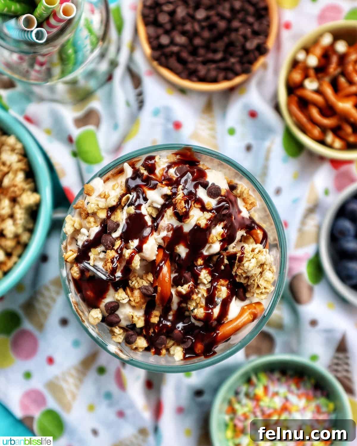 Ice Cream Parfait: A Symphony of Flavors and Textures 2 Ice cream parfait topped with granola, chocolate syrup, and mini chocolate chips on a colorful kitchen towel, surrounded by various toppings.