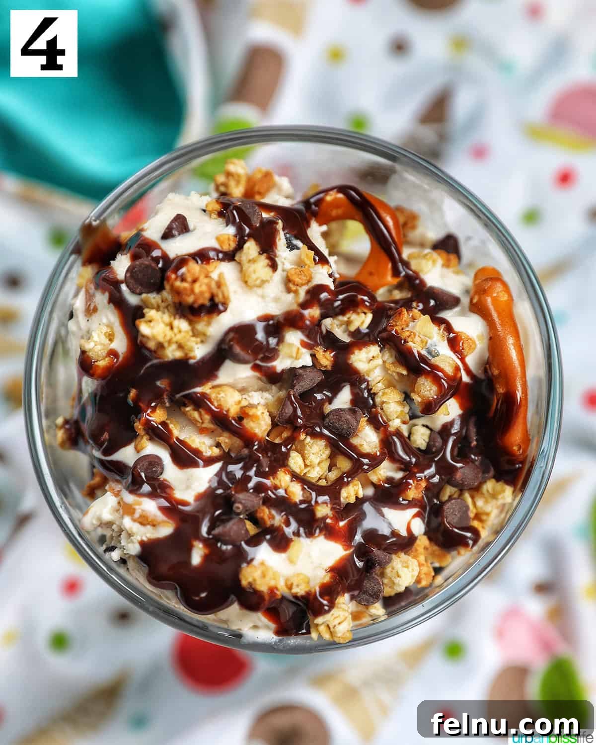 Ice Cream Parfait: A Symphony of Flavors and Textures 8 An ice cream parfait, generously topped with granola, chocolate syrup, and mini chocolate chips on a vibrant kitchen towel.