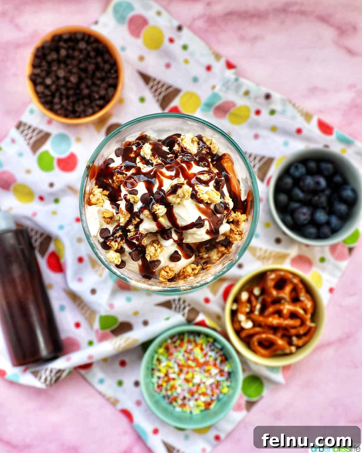 Ice Cream Parfait: A Symphony of Flavors and Textures 9 An ice cream parfait, topped with granola, chocolate syrup, and mini chocolate chips on a colorful kitchen towel, surrounded by various toppings.