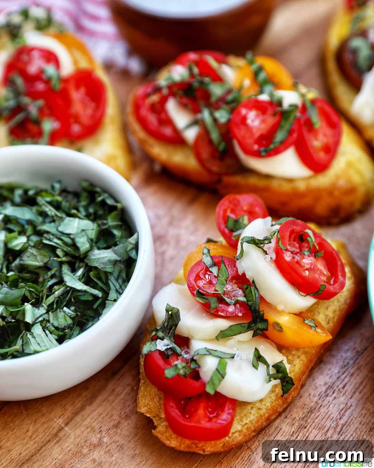 Elegant Caprese Crostini arranged on a wooden board, with a small bowl of fresh basil leaves beside it, suggesting fresh ingredients and stylish presentation.