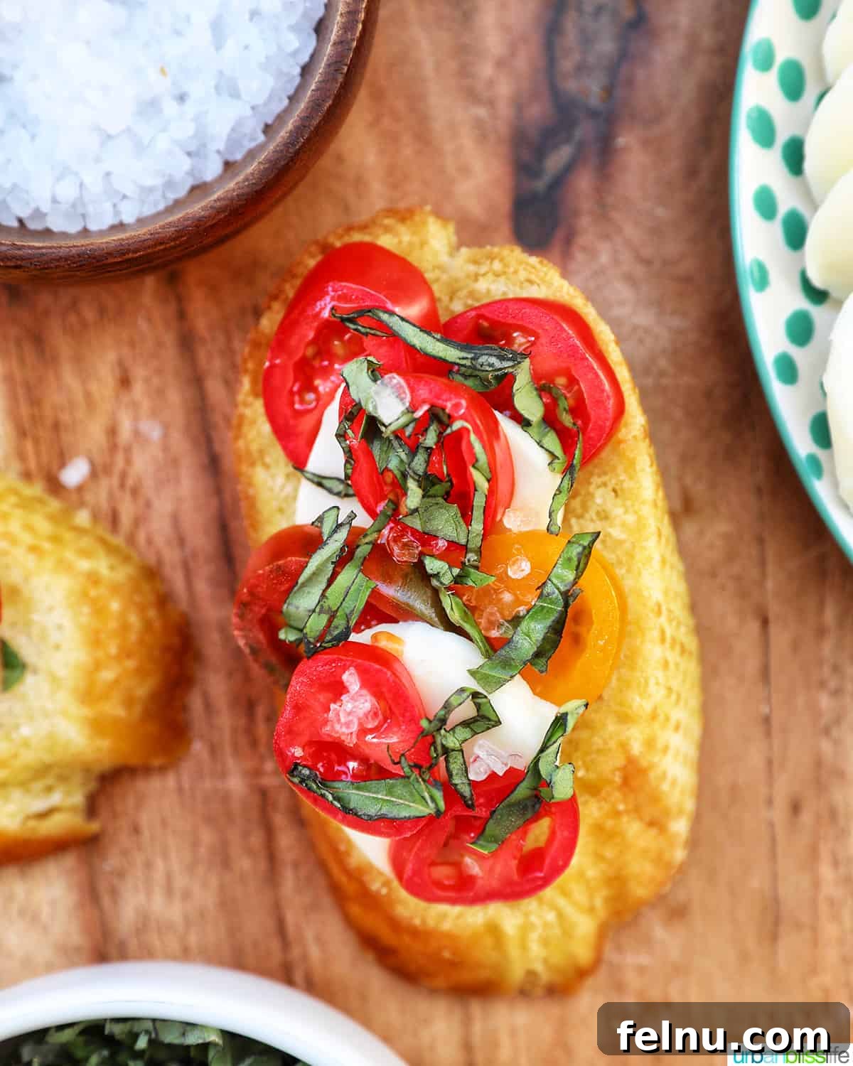 Close-up of a single Caprese Crostini slice, perfectly toasted and topped with mozzarella, sliced cherry tomato, and fresh basil, resting on a rustic wooden board.