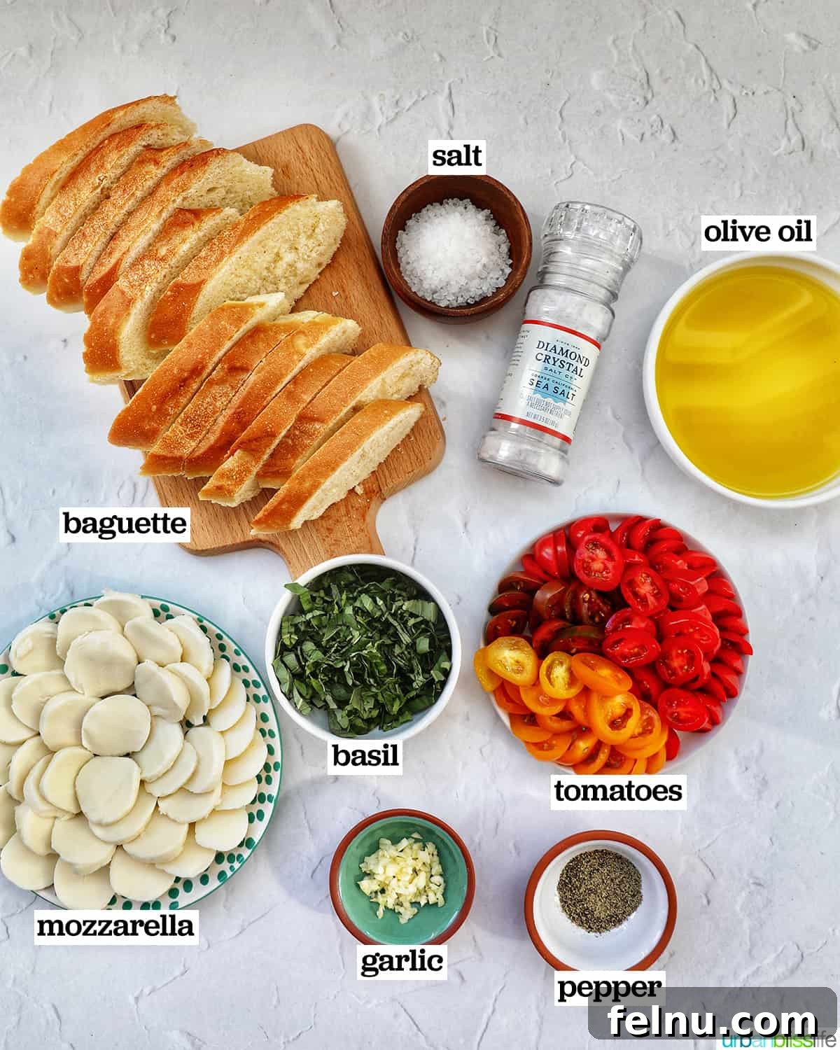 Various bowls holding ingredients for Caprese Crostini, including sliced tomatoes, fresh mozzarella balls, basil leaves, and olive oil.